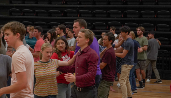 In a line around the floor, pairs of students practice leading each other