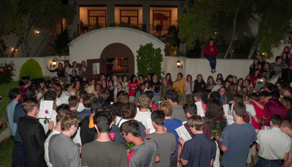 The men gather around the women's dorm entrance to sing, with roses in hands