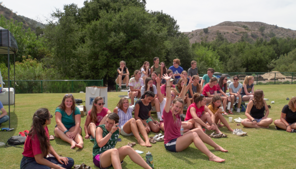 Non-playing students gather on the grass to the side of the field