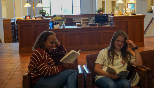 Two students in the armchairs afront the front desk, one smiling at to the camera