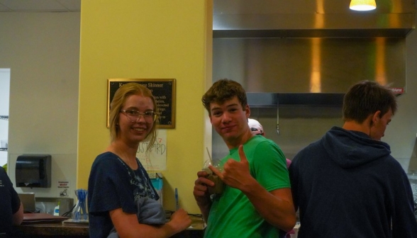 Three students. The middle one has a mocha in one hand, and makes the "hang loose" gesture with the other