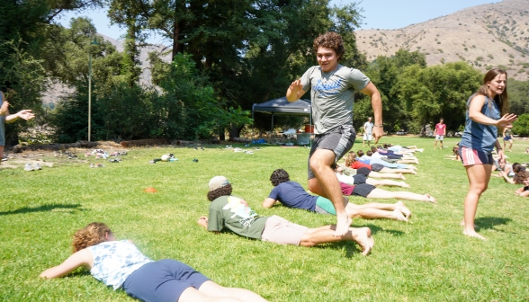 Mid-air, at the summit of a leap over another student lying on the grass