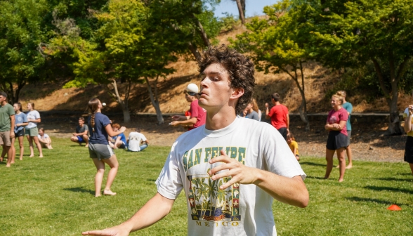 A student walks with utmost concentration. He is holding a spoon in his mouth, and in the spoon is an as-yet-unbroken egg.