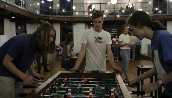 A tense game of foosball, while a student in a NASA T-shirt watches