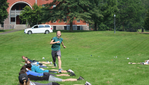 Students lie face down in a row as one student runs over them, trying not to step on any