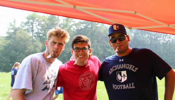 Three students in a row, with spoons in their mouths like pipes