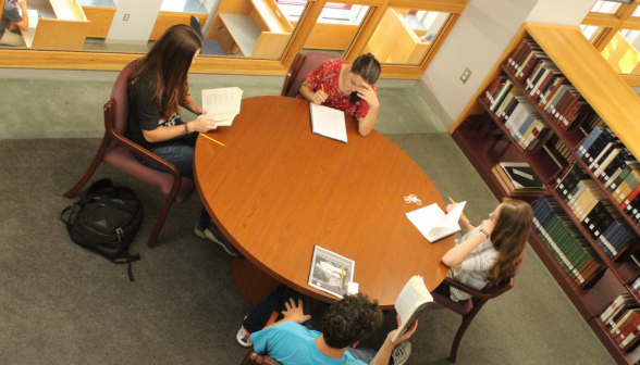 Overhead view: four study at a table by the stairs