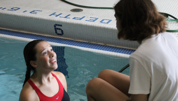 A student in the water talks to her friend sitting on the side