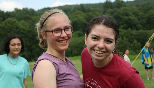 Two students smile for the camera afront the green New England hills