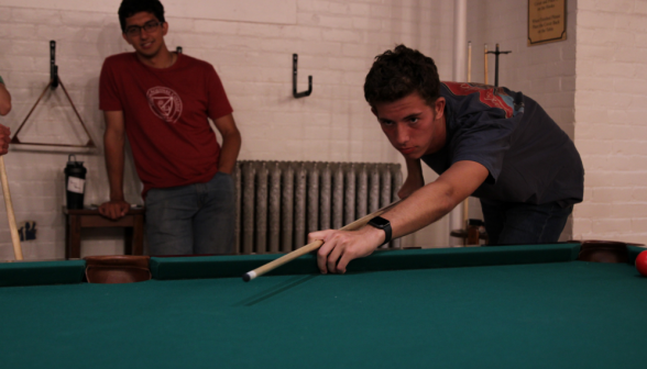 A student concentrates as they attempt a shot at the pool table