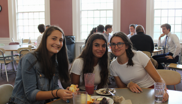 Three students pose at their table over lunch