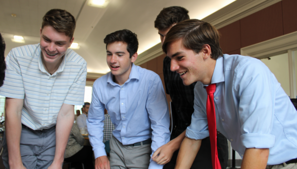 Four students lean over, looking at something or someone out of frame