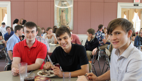 Three students, utensils in hand, pose for the camera at the lunch table