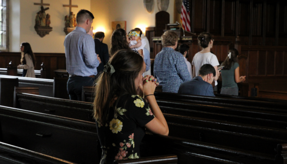 Students kneeling in the pews as a line forms behind the railing in the background