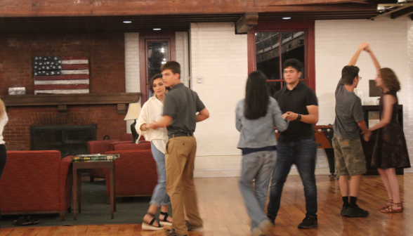 Three couples practice their moves afront the fireplace and armchairs