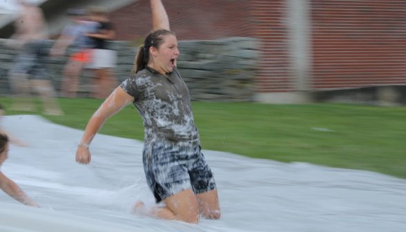 A student goes down the slide kneeling, arm in air