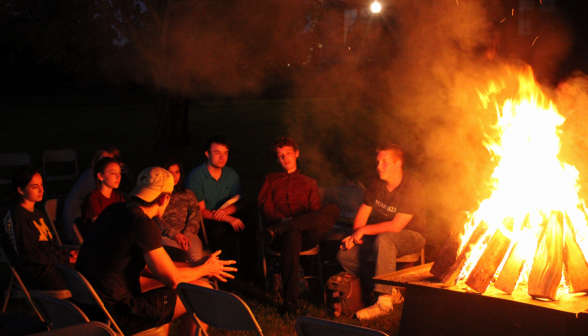 Closeup of a semicircle of student chatting on one side of the fire