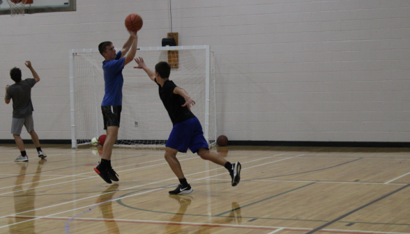 A student attempts to block another, who is making a shot on the basket
