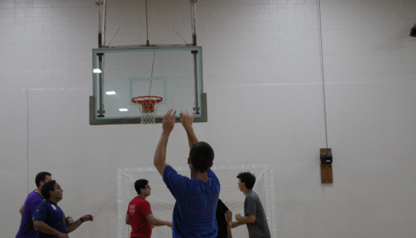 A student shoots for the basket, while others rush in to catch the rebound