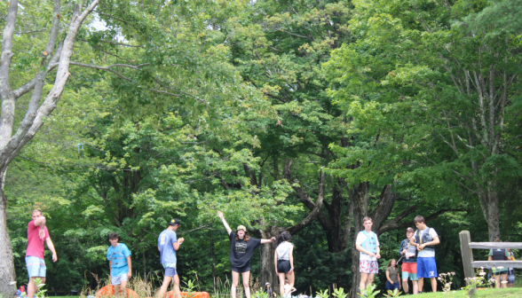 Eight students at the water's edge, putting on life vests and pointing at the camera