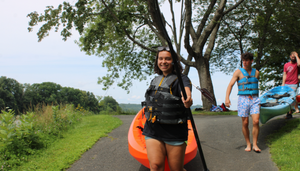 Two pairs of students haul their respective kayaks down the the water