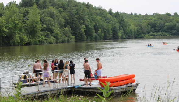 A large group of students on a short pier, launching kayaks