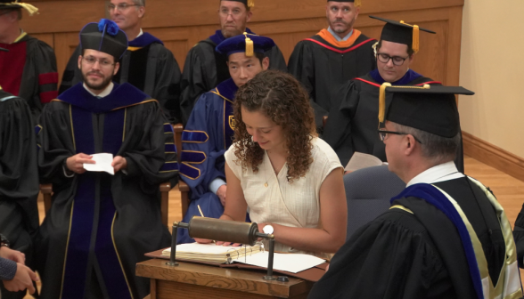 A student, smiling slightly, sets down her signature in the register
