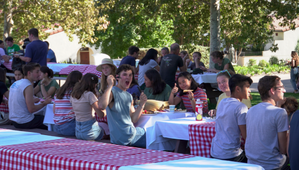Students eat at long tables with checkered tablecloths