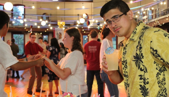 A student turns to the camera, lemonade in hand, with the dancefloor in view behind