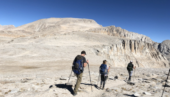 Three trek along a barely-visible path beside a rocky sheer face