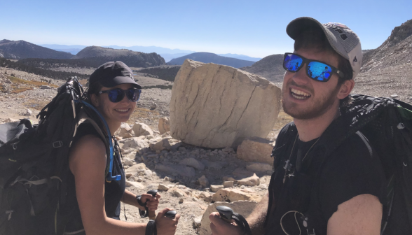 Two students pose for a picture afront a large boulder and a rocky plain