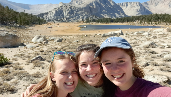 Three girls in a selfie afront a lake and the hills in the distance
