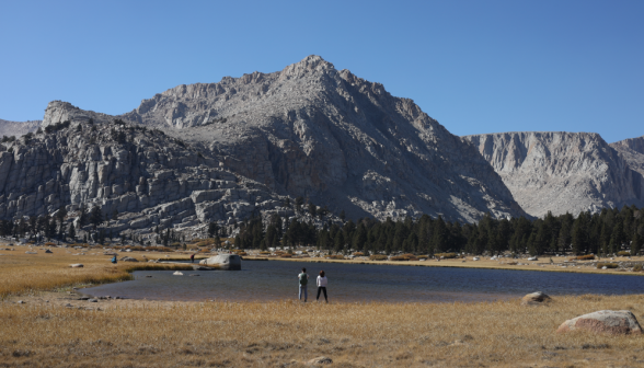 Two students stand afront the lake, looking out over the hills