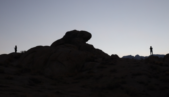 Two students on the ridge, separated by a large outcropping, silhouetted against the sunrise
