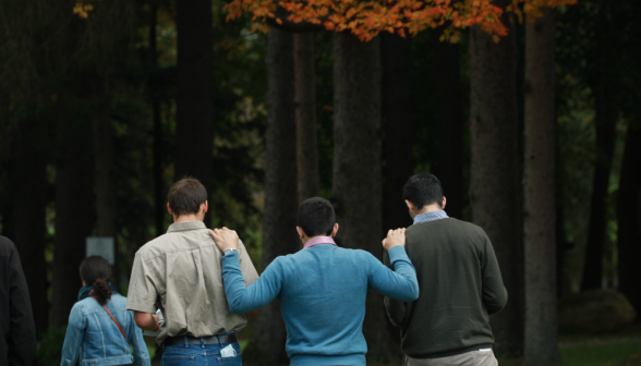 Three students walk in a row, the middle one with a hand on the shoulder of either of his companions