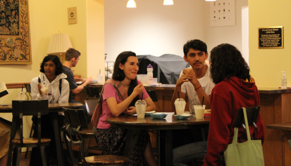 Three students chat at one of the tables