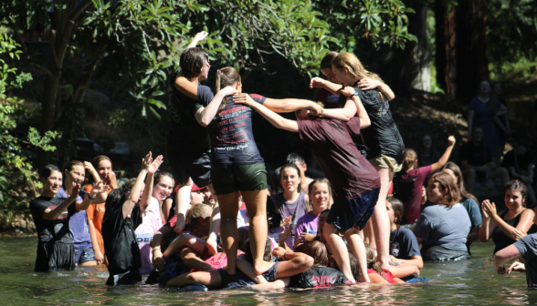 In the pond, six women carefully balance atop the interlinked arms of their comrades