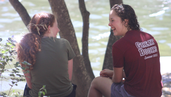 Two girls laugh and chat on the side of the pond