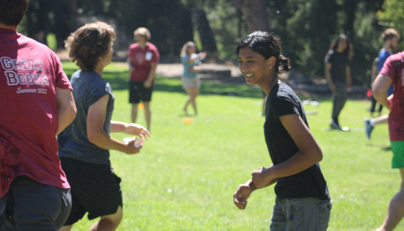 On the right, a laughing student turns toward the camera, while a student on the left prepares a water-balloon throw