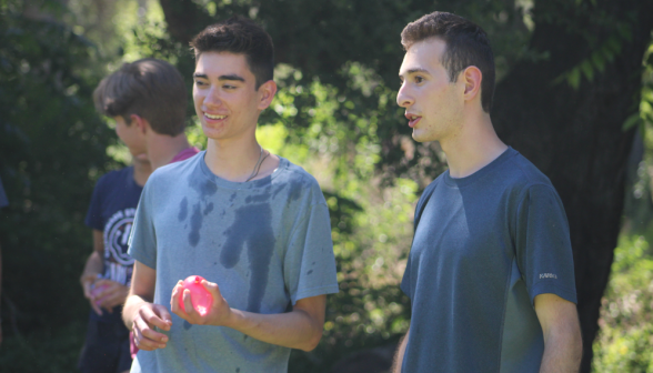 Two students, one with water balloon in hand, plan their strategy
