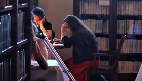 Students study at a table, half-hidden by a bookcase