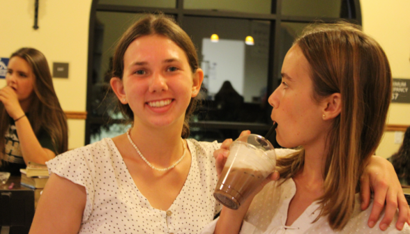 Two students: one looks at the camera, the other, drink in hand, at the first