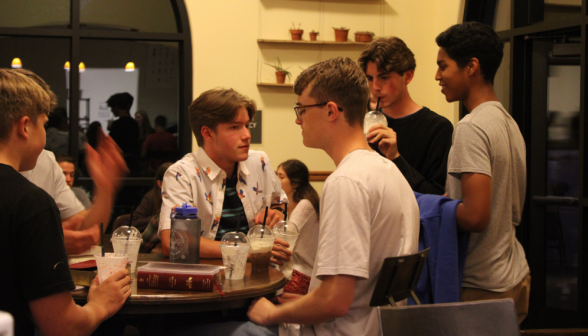A group of students chats at one side of a table