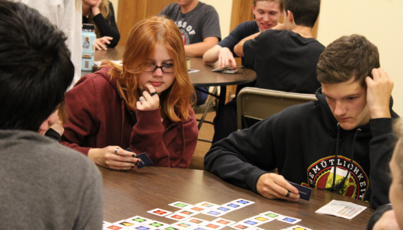 A group of students around a table play a Qwirkle-like card game