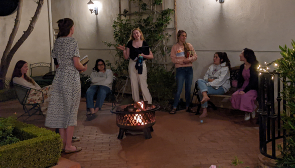 Seven girls chat around an outdoor fire