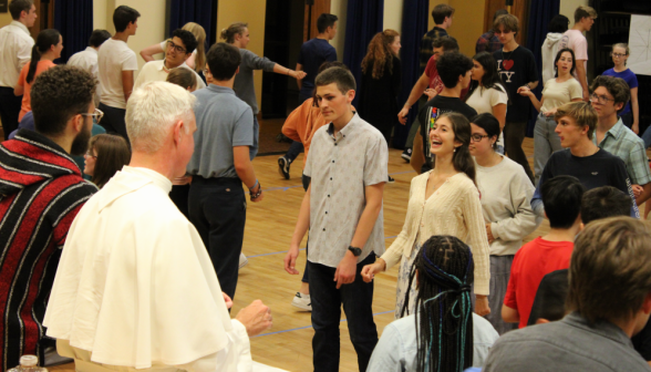 Students practice in the background; in the foreground, Fr. Walshe looks on