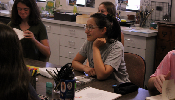 A student surrounded by her friends and drawing equipment at the art table