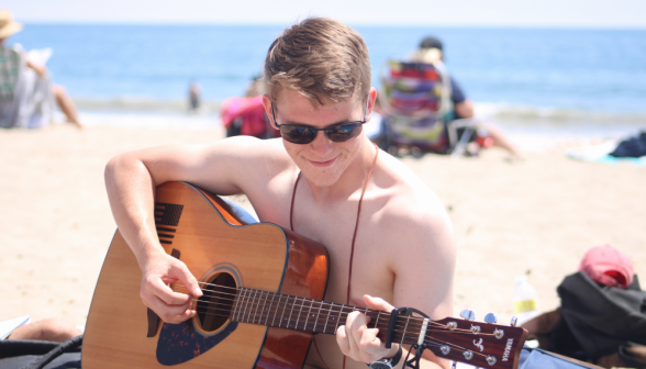 A student on the beach breaks out their guitar
