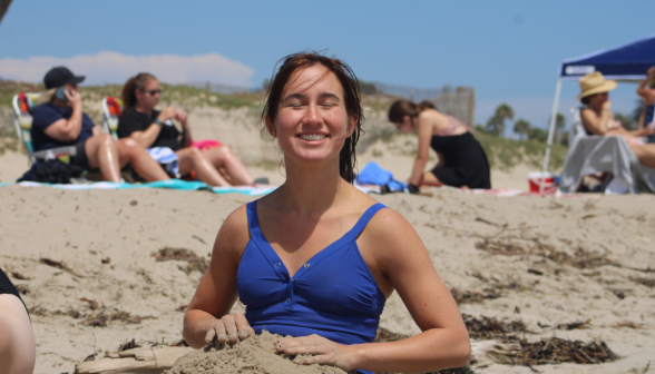 A student half-buried in sand smiles for the camera