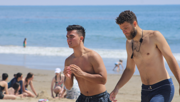 Two students - one sporting an excellent beard - walk along the beach